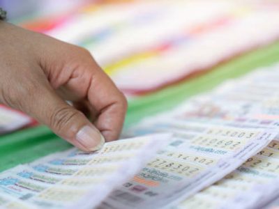 Asian woman hand holds of choose pile of Thailand lottery in blur bright sunlight. Close up, selective focus.