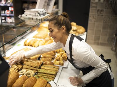 Woman preparing pastry for sale in supermarket bakery department.